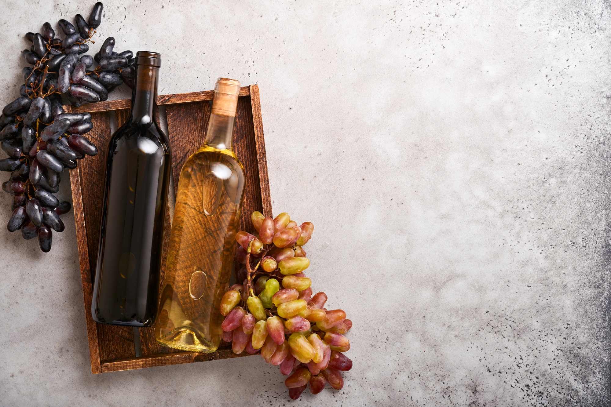 Two Wine bottles with grapes and wineglasses on old gray concrete table background with copy space.